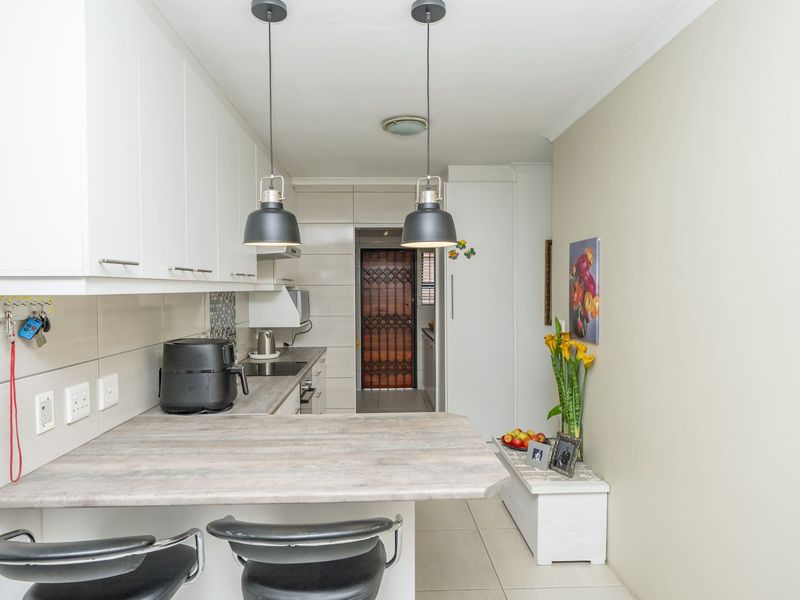 A modern, well-maintained kitchen featuring white cabinetry, a breakfast bar, tiled backsplash, and contemporary pendant lighting.
