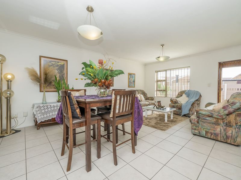 Spacious open-plan living and dining area featuring neutral tiled flooring, large windows with venetian blinds, and direct access to the exterior.