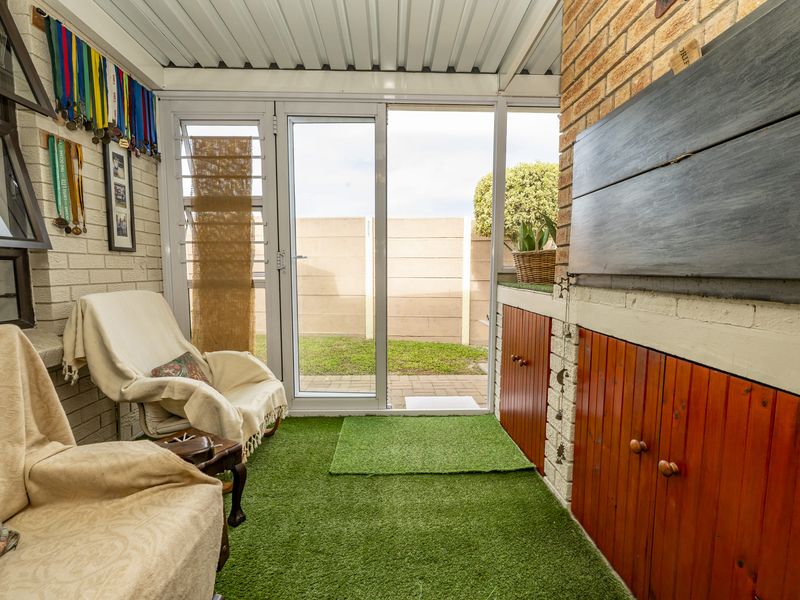 Covered patio area featuring a built-in braai, brick wall finishes, and direct access to the rear garden through sliding glass doors.