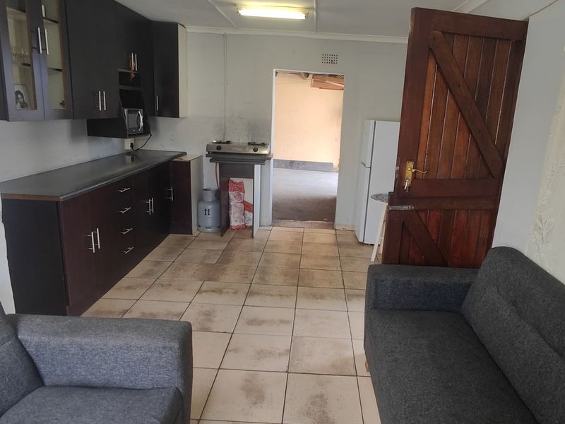 Open plan living and kitchen area featuring dark cabinetry, tiled flooring, and direct access to an adjacent utility space.