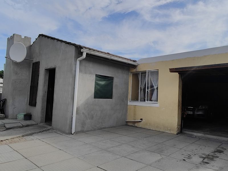 Rear exterior view showing a paved patio area, carport, and a mix of plastered and painted wall finishes.