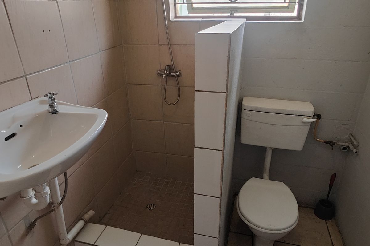 A functional bathroom featuring a pedestal basin, a tiled shower enclosure, and a toilet, requiring cosmetic updates to improve its overall condition and aesthetic.