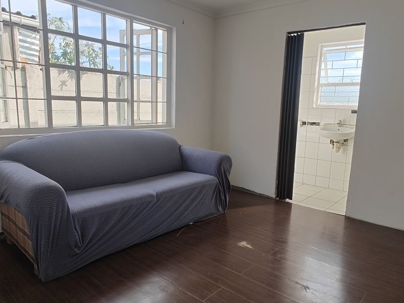 A bedroom featuring laminate flooring and grid-pattern windows, with an adjoining small bathroom area accessible via a folding door.