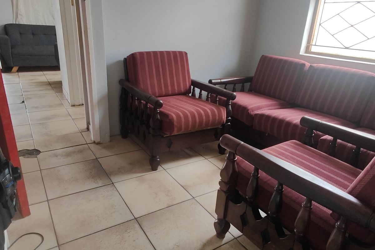 A living room area featuring ceramic floor tiles and a diamond-pattern window, showing signs of wear and dated finishes.
