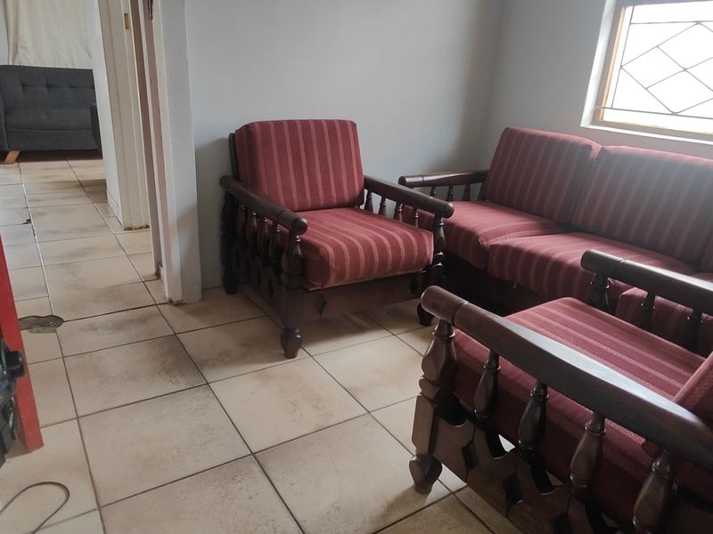 A living room area featuring ceramic floor tiles and a diamond-pattern window, showing signs of wear and dated finishes.