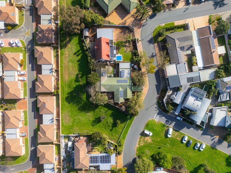 Aerial view of a residential property featuring a tiled roof with solar panels, a swimming pool, and surrounding landscaped garden areas.