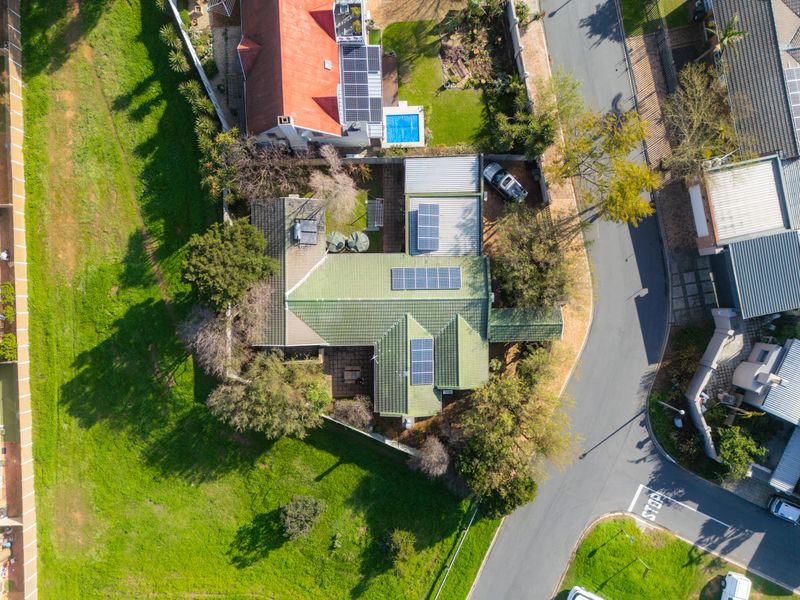 Aerial view of the property showcasing the roof structure, installed solar panels, swimming pool, and surrounding garden area.