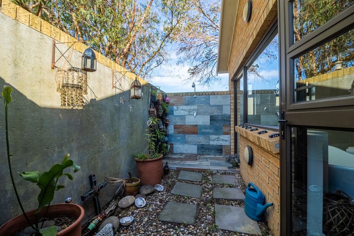 A private outdoor courtyard featuring a built-in shower, brick and tiled wall finishes, and paved pathways, offering a secluded space for relaxation.