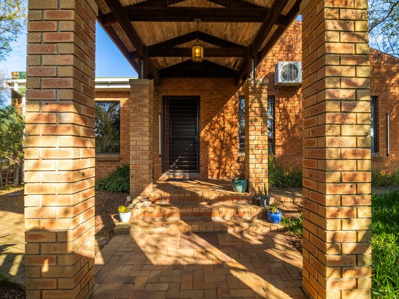 A welcoming front entrance featuring a covered porch with brick pillars, timber ceiling detail, and a secure entrance door.