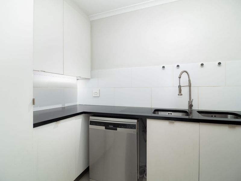 A clean and functional scullery featuring modern white cabinetry, black stone countertops, a double stainless steel sink, and an integrated dishwasher.