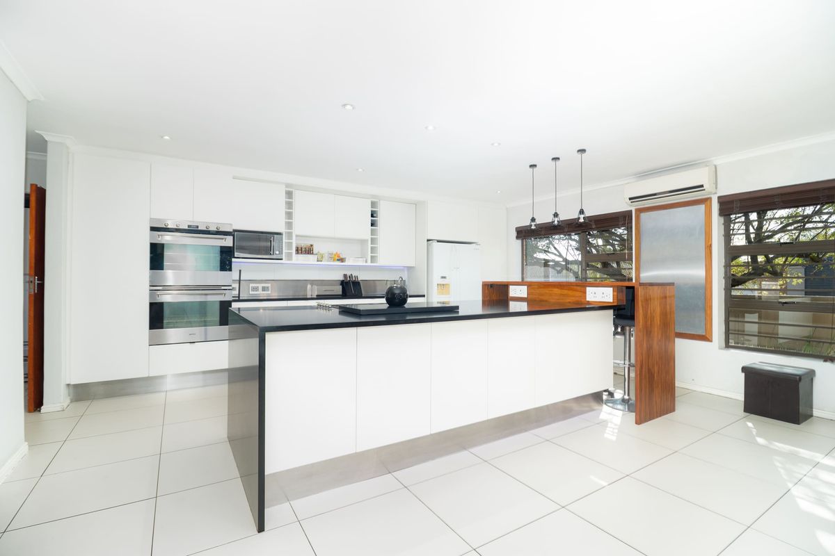 Modern kitchen featuring a large central island with stone countertops, built-in double oven, microwave, and sleek white cabinetry with tiled flooring.