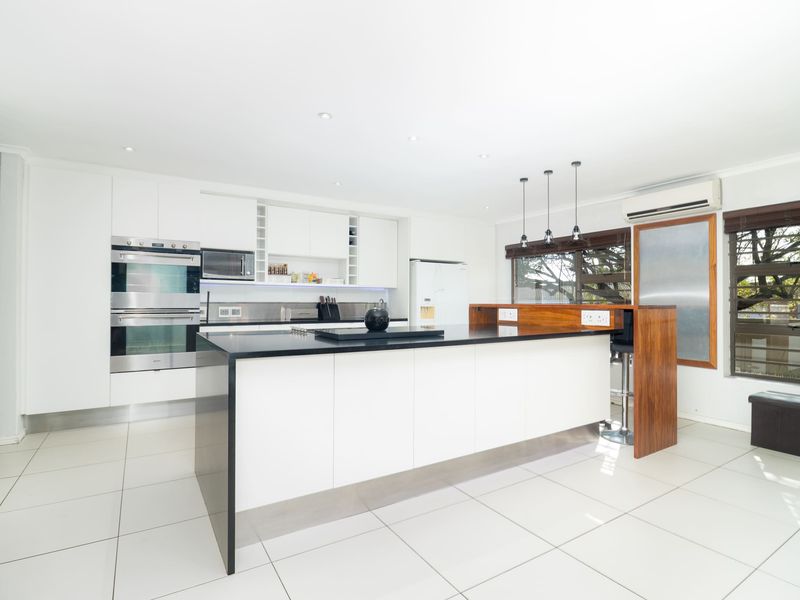 Modern kitchen featuring a large central island with stone countertops, built-in double oven, microwave, and sleek white cabinetry with tiled flooring.