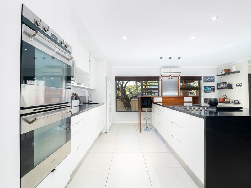 Modern kitchen featuring a large island with gas cooktop, sleek white cabinetry, stone countertops, and a built-in double oven.