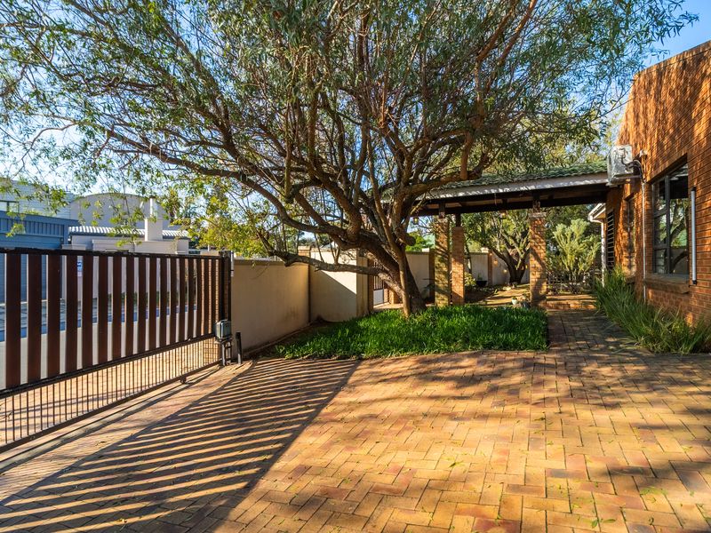 Front entrance area featuring brick paving, a secure sliding gate, and a covered walkway leading to the main building structure.