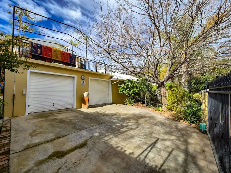 Front exterior view featuring a double garage with roller doors and an upper-level balcony with metal railings, set within a landscaped garden area.