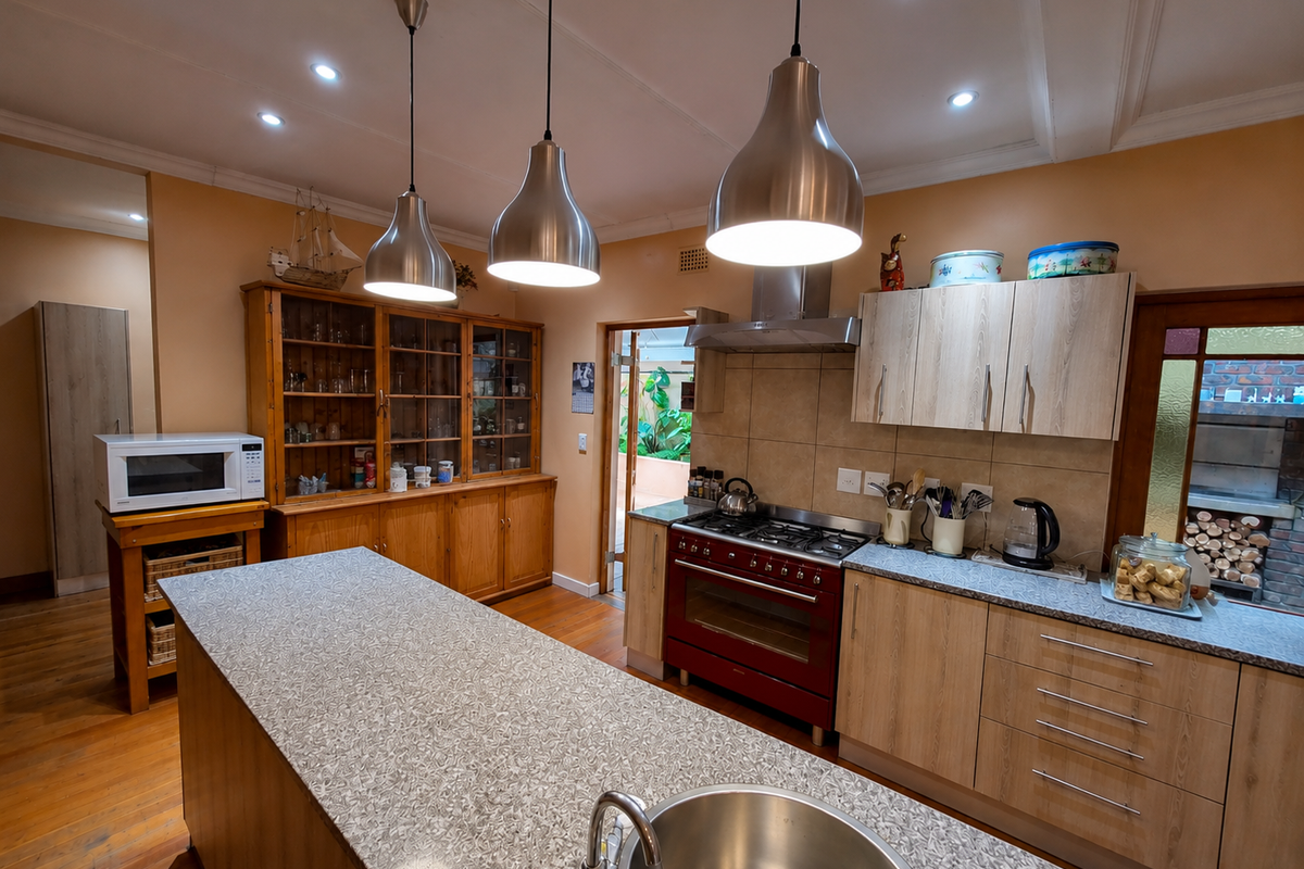 Spacious kitchen featuring a large island with sink, gas range, stainless steel extractor, ample cabinetry, and warm hardwood flooring with recessed and pendant lighting.