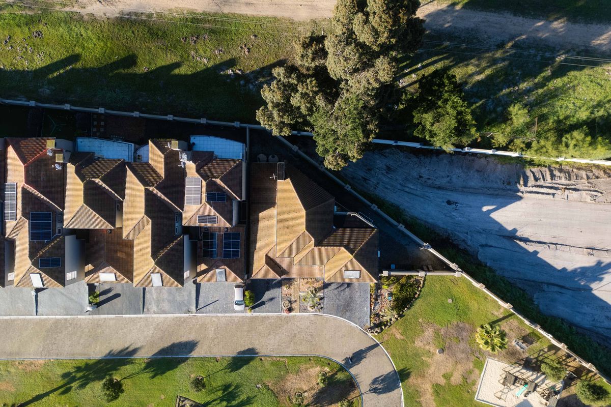 Aerial view of the property showcasing the tiled roof with integrated solar panels, paved driveway, and surrounding landscaped garden areas.