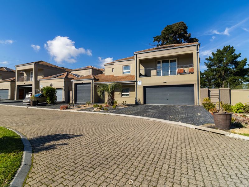 Front elevation of a modern residential townhouse featuring a paved driveway, double garage, and an upper-level balcony with metal railings.