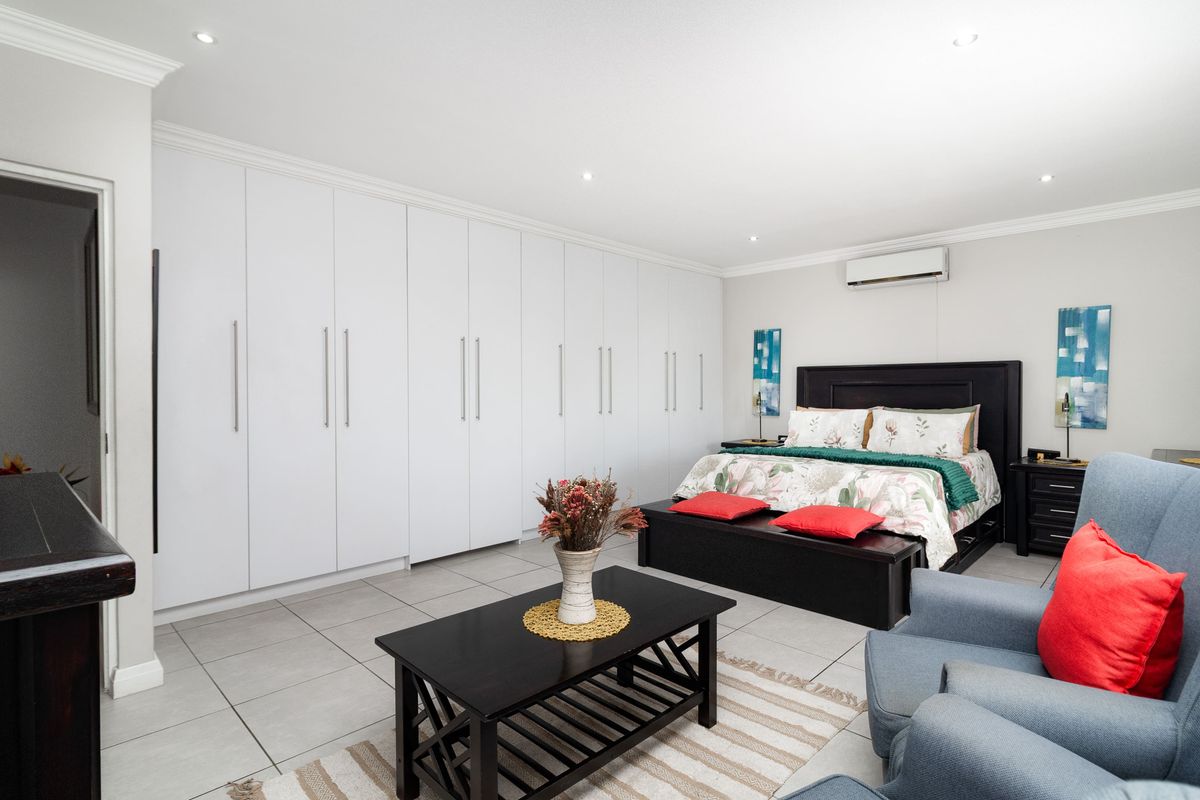 Spacious bedroom featuring extensive floor-to-ceiling built-in cupboards, tiled flooring, recessed lighting, and a wall-mounted split-system air conditioner.