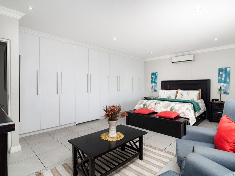 Spacious bedroom featuring extensive floor-to-ceiling built-in cupboards, tiled flooring, recessed lighting, and a wall-mounted split-system air conditioner.