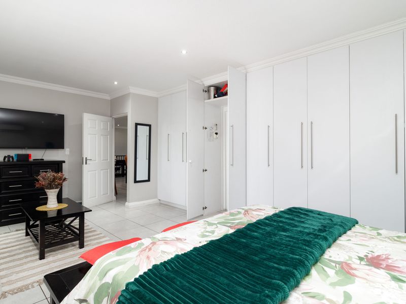 Spacious bedroom featuring extensive white built-in cupboards, neutral tiled flooring, and modern recessed lighting.