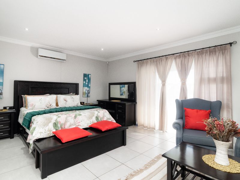 Spacious bedroom featuring tiled flooring, recessed downlighting, and a wall-mounted split-system air conditioner, with direct access to natural light through large window coverings.