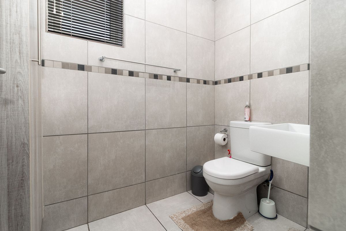 A clean and modern bathroom featuring neutral large-format wall and floor tiles, a wall-mounted basin, and a standard toilet.