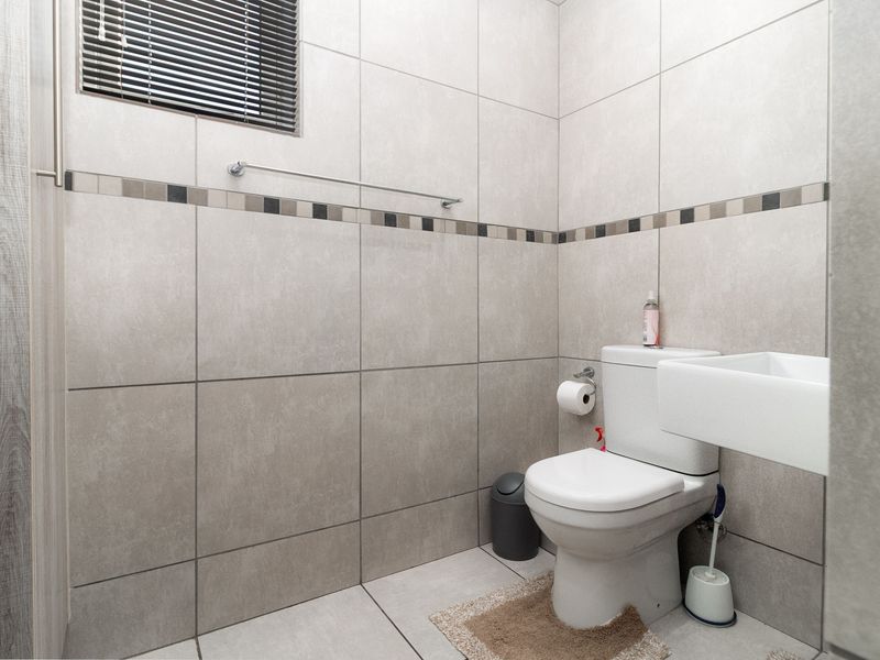 A clean and modern bathroom featuring neutral large-format wall and floor tiles, a wall-mounted basin, and a standard toilet.