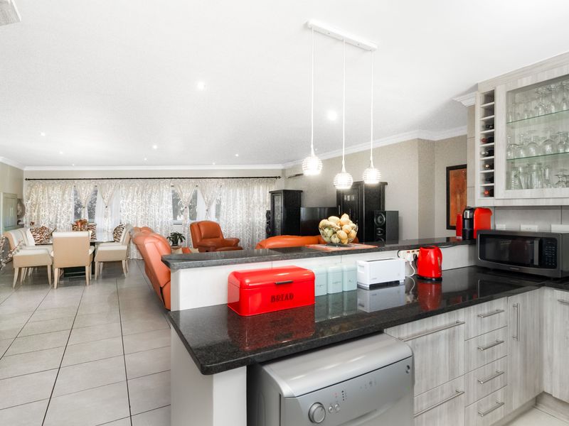 Open-plan living and kitchen area featuring modern cabinetry, granite countertops, tiled flooring, and integrated display shelving, creating a functional and cohesive living space.