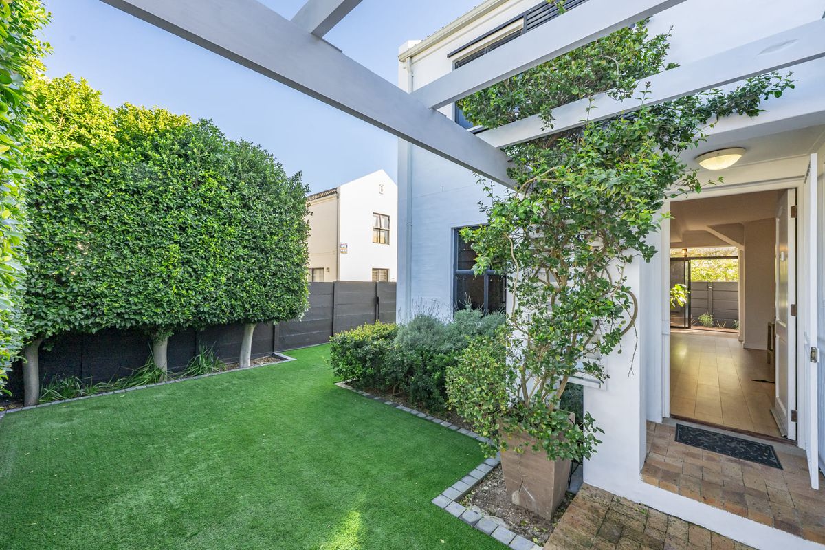A well-maintained rear garden featuring an artificial lawn, brick paving, and a timber pergola, providing a seamless transition to the interior living space.