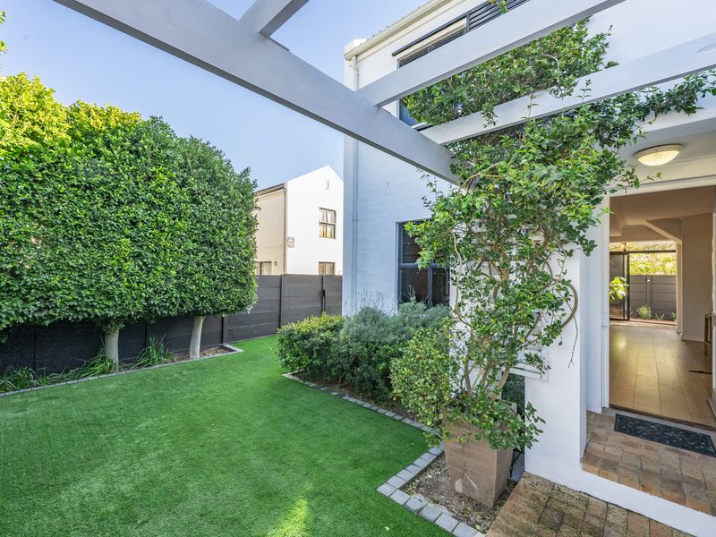 A well-maintained rear garden featuring an artificial lawn, brick paving, and a timber pergola, providing a seamless transition to the interior living space.