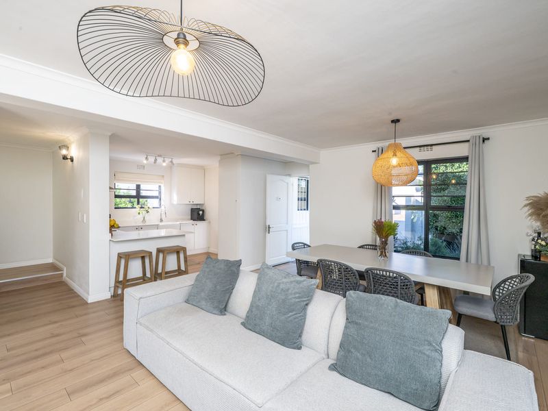 Bright open-plan living and dining area featuring laminate flooring, modern kitchen with stone countertops, and stylish pendant lighting throughout the space.