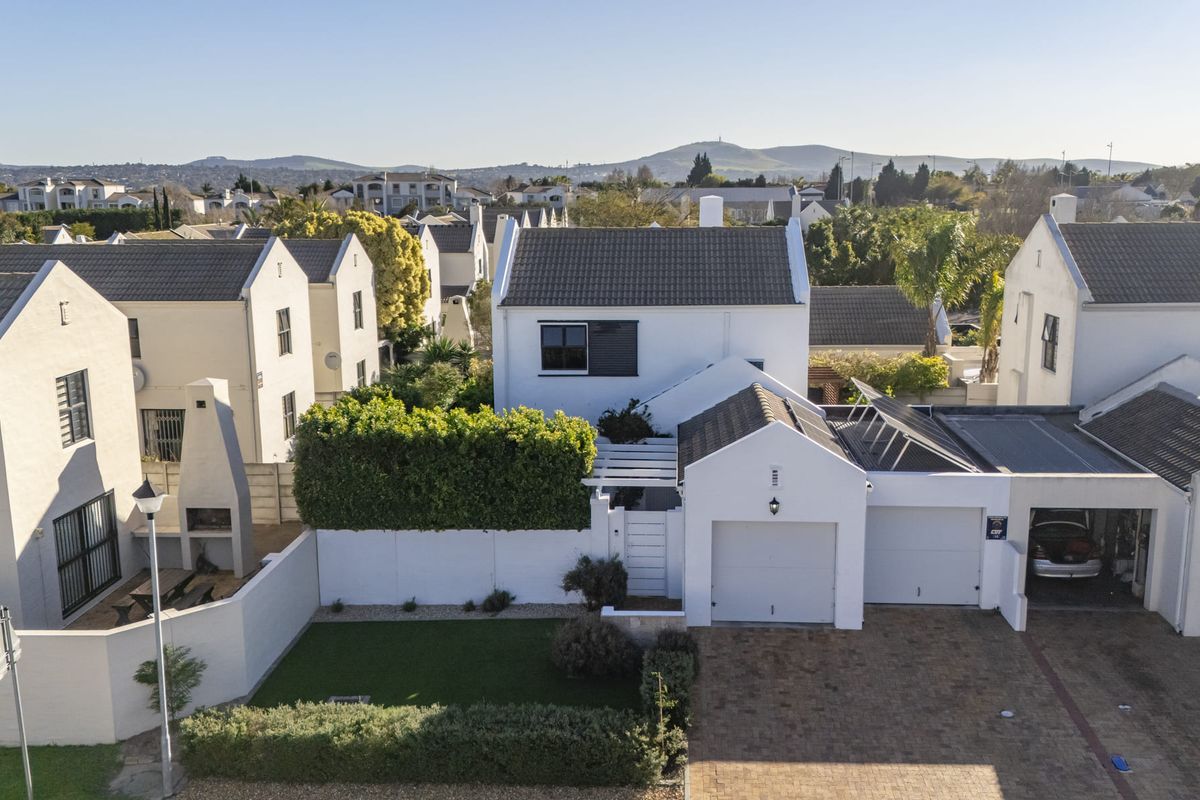 Aerial view of a residential property featuring a double garage, paved driveway, outdoor fireplace, and solar panels within a well-maintained estate setting.