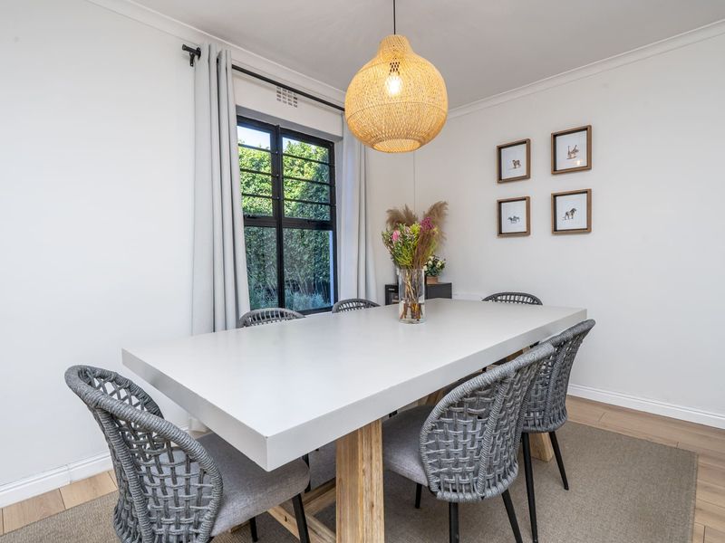 A bright and well-maintained dining room featuring a large black-framed window, neutral walls, and modern timber-look flooring.