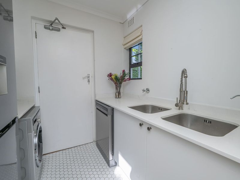 A clean and functional laundry room featuring double stainless steel sinks, stone countertops, modern cabinetry, and stylish hexagonal floor tiles.