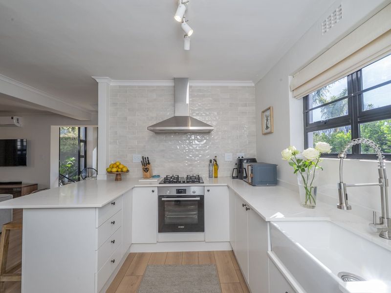 Modern kitchen featuring white cabinetry, quartz countertops, a farmhouse sink, subway tile backsplash, and integrated stainless steel appliances.