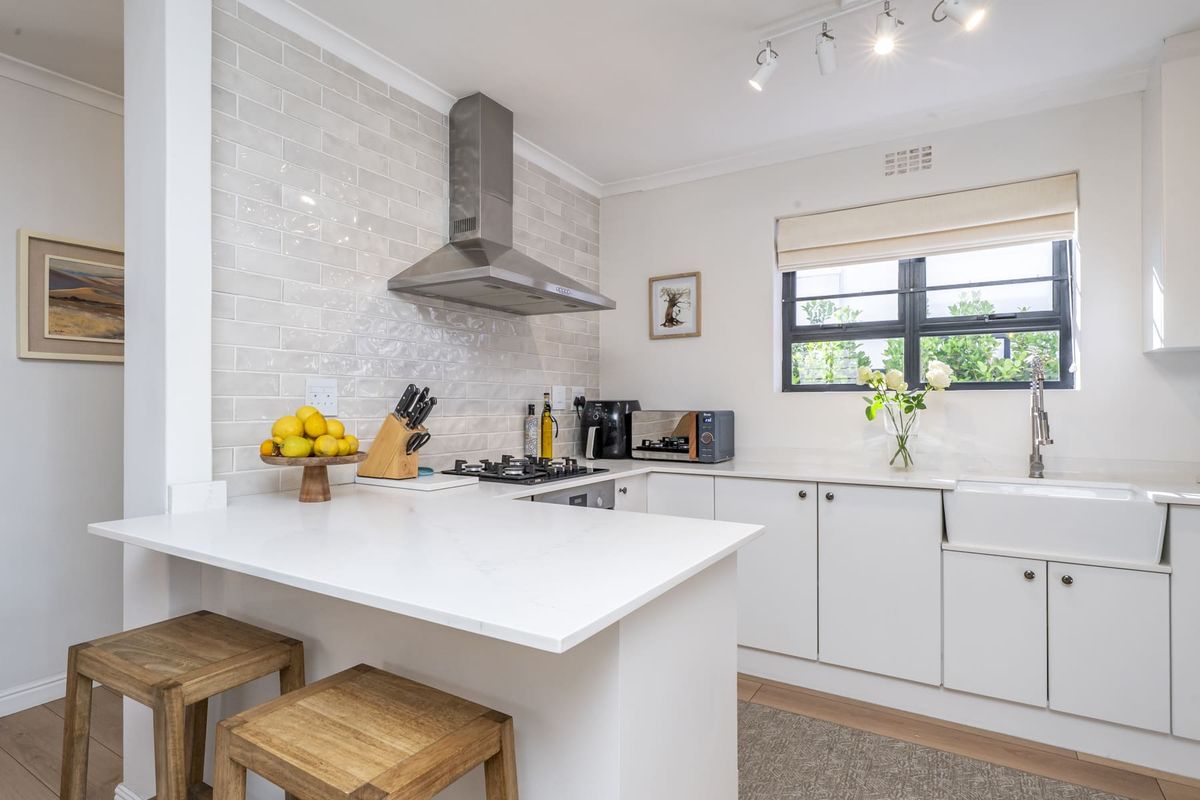 Modern kitchen featuring white cabinetry, quartz countertops, a farmhouse sink, subway tile backsplash, and a stainless steel extractor fan.