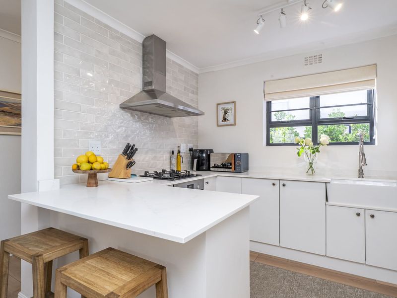 Modern kitchen featuring white cabinetry, quartz countertops, a farmhouse sink, subway tile backsplash, and a stainless steel extractor fan.