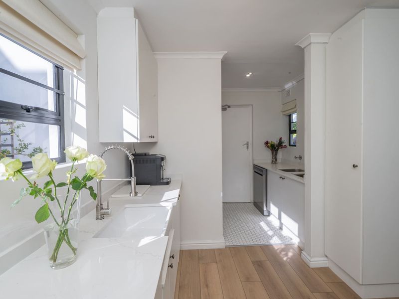 A bright and modern scullery featuring clean white cabinetry, quartz countertops, an undermount sink, and a mix of tiled and laminate flooring.
