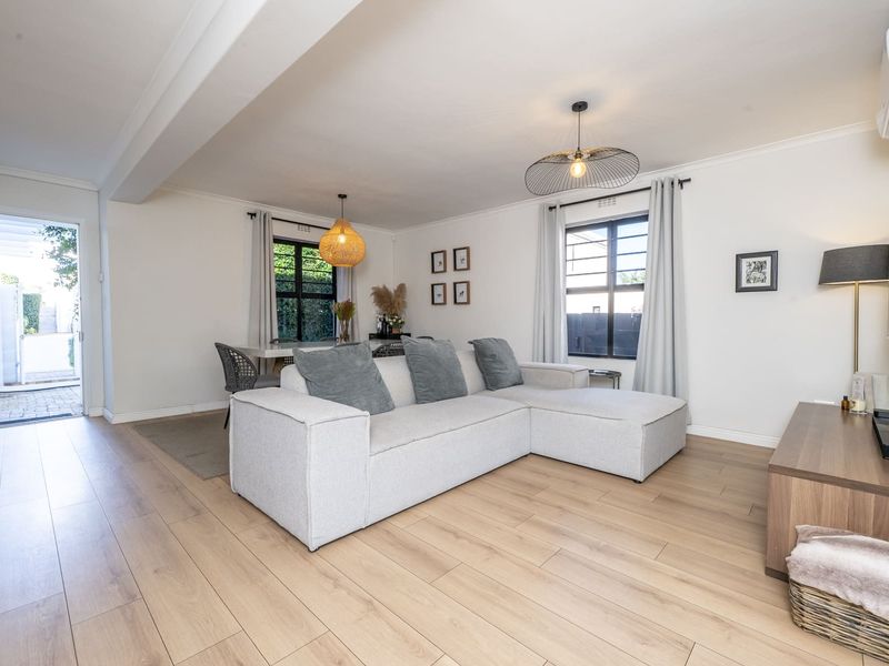 Bright open-plan living and dining area featuring light laminate flooring, modern pendant lighting, and direct access to an outdoor patio space.