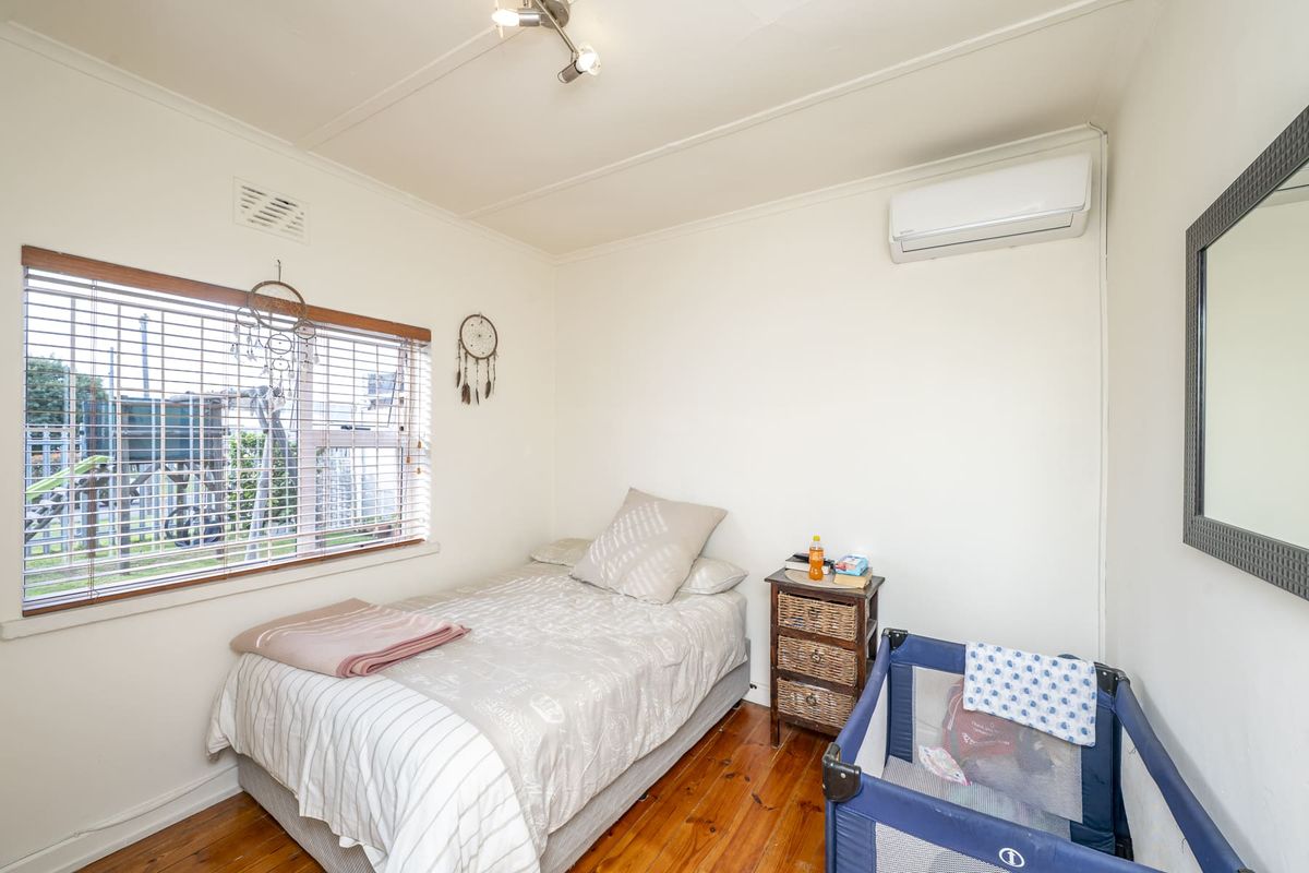 A functional bedroom featuring polished timber flooring, a wall-mounted split-system air conditioner, and natural light through venetian blinds.