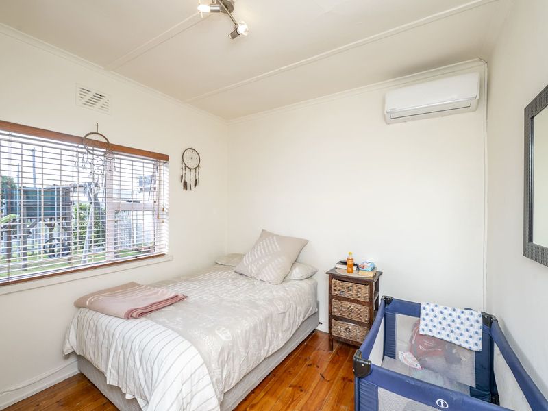 A functional bedroom featuring polished timber flooring, a wall-mounted split-system air conditioner, and natural light through venetian blinds.