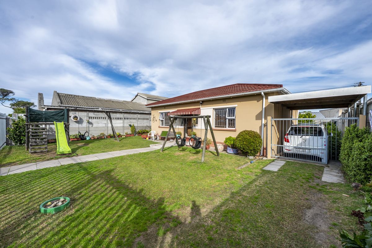 Rear view of the property featuring a lawn, paved walkway, carport, and secure boundary walling.