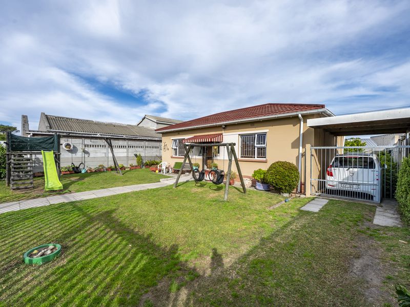 Rear view of the property featuring a lawn, paved walkway, carport, and secure boundary walling.
