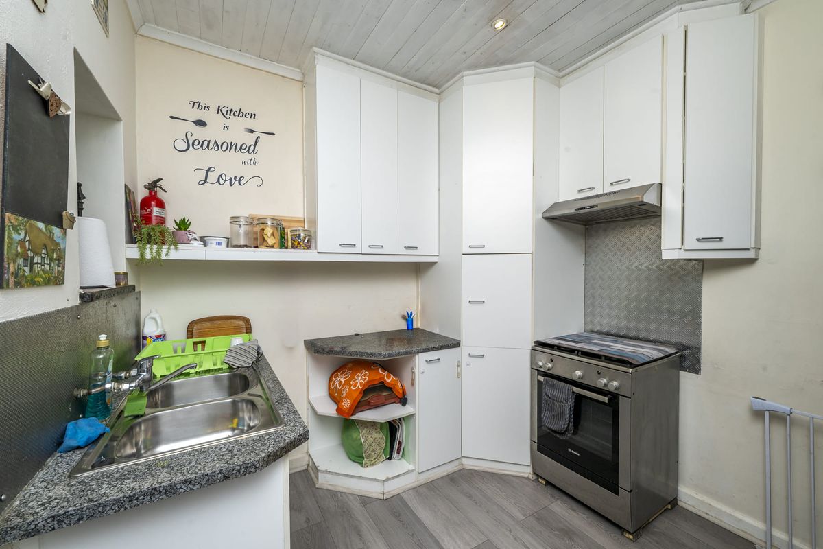 Compact kitchen featuring white cabinetry, stainless steel sink, freestanding oven with extractor fan, and durable laminate flooring.