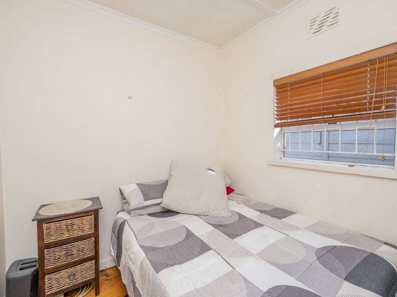 A compact bedroom featuring timber flooring, a window with security bars and venetian blinds, and neutral wall finishes.
