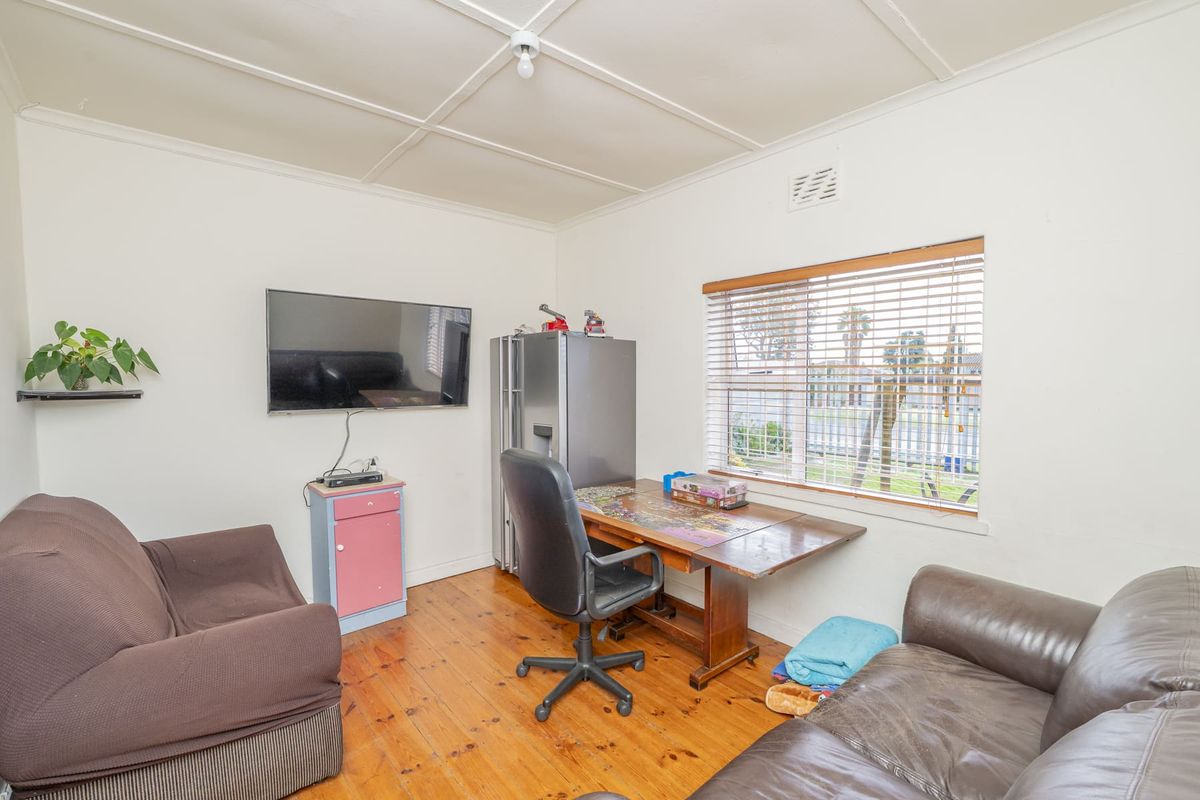 A multi-purpose living space featuring original timber flooring, large window with venetian blinds, and a functional layout suitable for a home office or lounge.