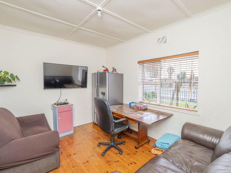 A multi-purpose living space featuring original timber flooring, large window with venetian blinds, and a functional layout suitable for a home office or lounge.