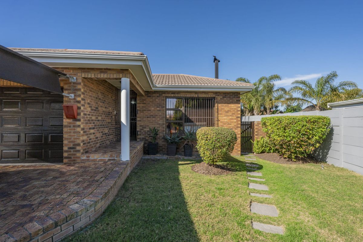 Rear exterior view of a face brick house featuring a paved patio area, small garden, and secure boundary walling.