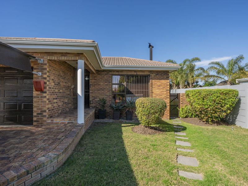 Rear exterior view of a face brick house featuring a paved patio area, small garden, and secure boundary walling.